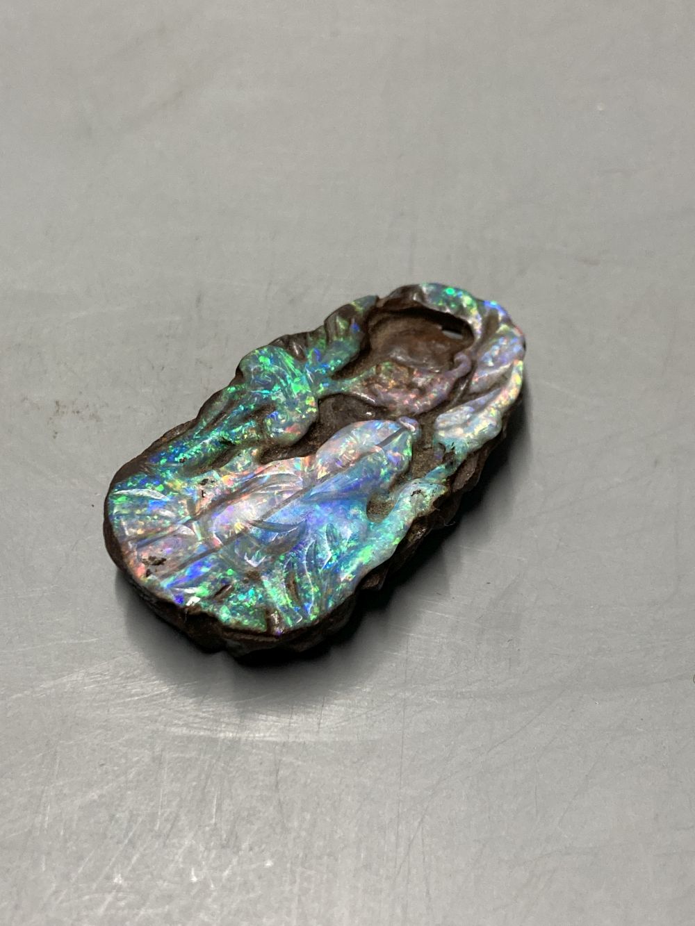 A Chinese carved Australian boulder opal pendant with flowers to the front and fruit to the back, 4.5cm, gross 17.1 grams.